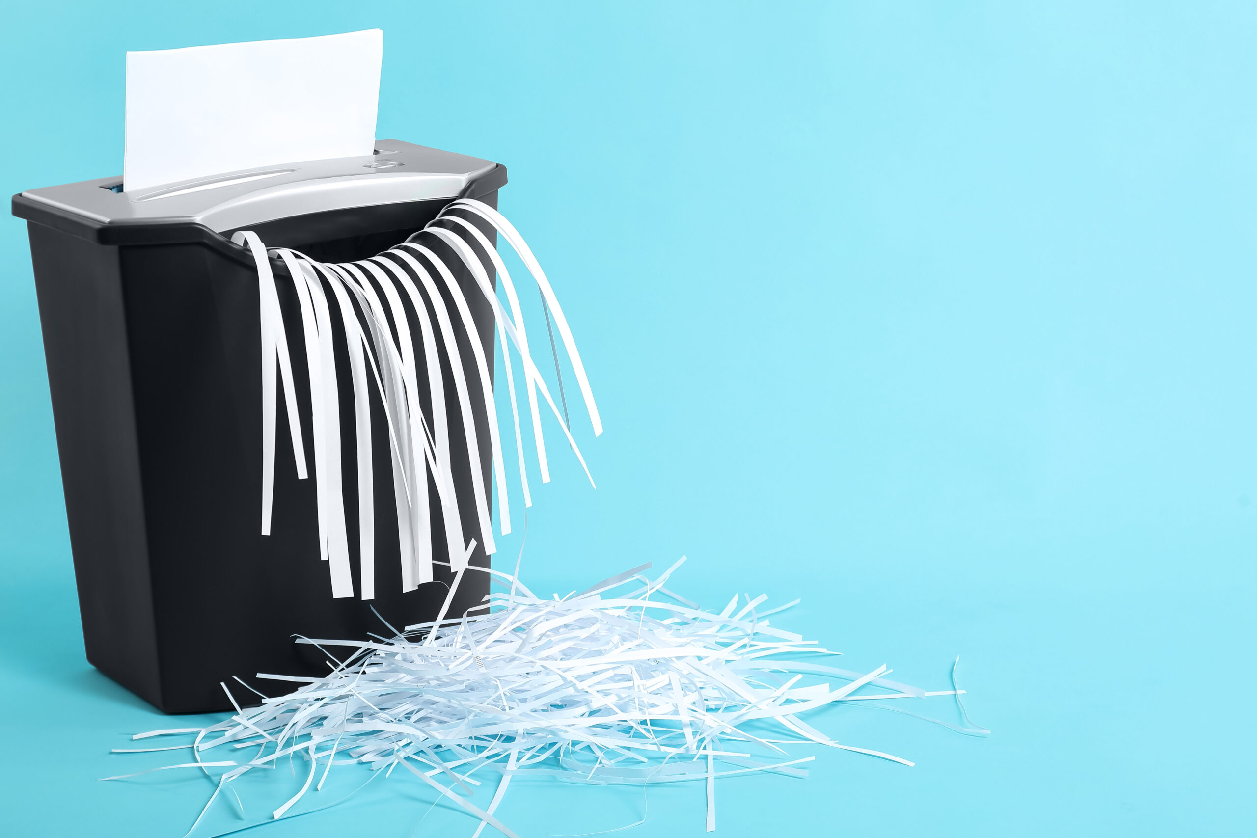 Destroying sheet of paper with shredder on light blue background, space for text