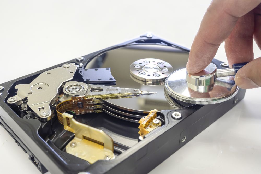 A person holds a stethoscope against the magnetic platter of an open hard disk drive, illustrating secure hard disk disposal.